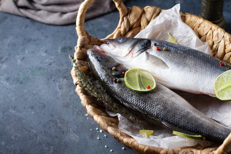 Raw sea bass. A pair of fish in a wicker basket with spices and lime. Close-up, copy spaseの写真素材
