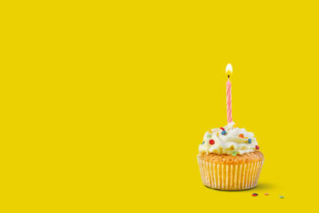 Yellow background with festive cupcake with burning candleの写真素材