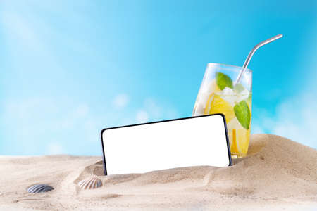 Smartphone with cut out white screen, copy space on the sand at the beach, summerの写真素材