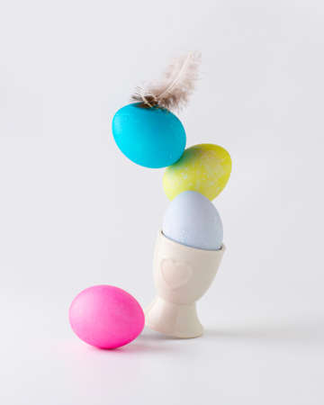 Multicolored Easter eggs and a feather balance on an egg stand