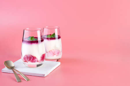 Dessert in a glass of panna cotta from cream and red orange on a pink background, copy space