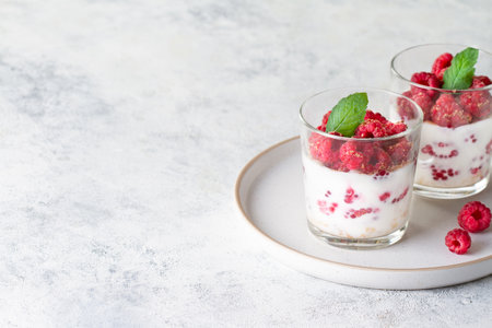 Two desserts in a glass with yogurt and raspberries on a gray background, copy space