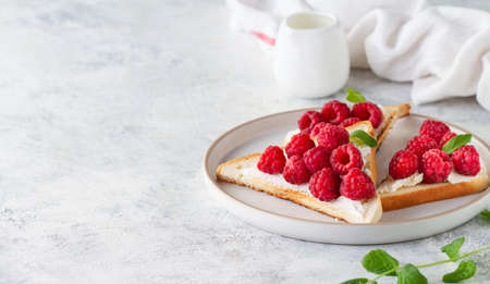 Sweet toasts with raspberries and cheese on a plate on the table, copy spaceの写真素材