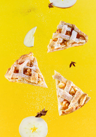 Pieces of american apple pie with cinnamon and powdered sugar levitate on a yellow background,...