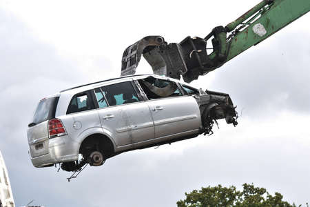 Car in a scrap yard being lifted by a mechanical grabber crane to be scrappedの写真素材