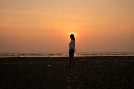 silhouette girl standing on beach on sunset backgroundの写真素材