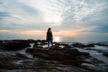 Woman standing on rock on the sea to see sunset viewの写真素材