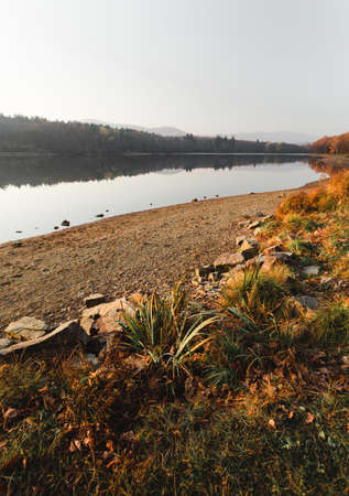 Beautiful scenic landscape with crystal blue water in lake (pond) on autumn day. Rocks and stone on the bank (beach) with natural sunlight - sunset fall shot.の写真素材