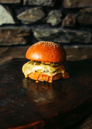 Illuminated photo of american hamburger with chuck roll meat, cheddar cheeese and other ingredietns on dark background.の写真素材