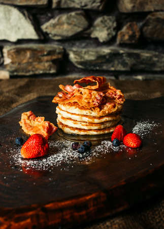 Tasty pancakes with strawberries, syrup, sugar and bacon on the top - darke background. Pancakes with fruits on dark wooden table.の写真素材