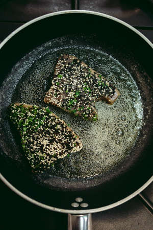 Fresh raw tuna fish steaks with pepper and other ingredients prepared for cooking. Roasted tuna fish in the frying pan on dark backgorund.の写真素材