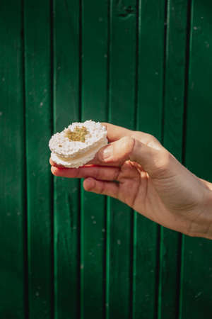 Female holding a cake in hand - green and dark background. Small tasty desserts.の写真素材