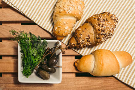 Lox, croissants, cream, capers and other ingredients prepared to cooking - top view. Traditional French croissants sandwich with fillet of salmon fish, soft cheese and capers on wooden background.の写真素材