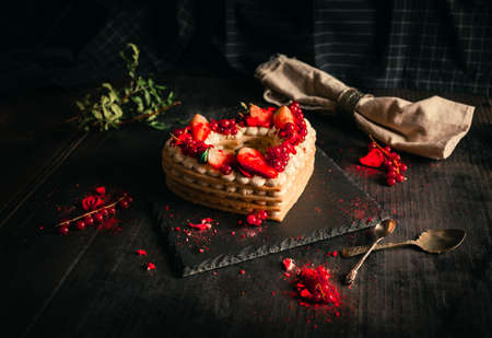 Confectionery concept - red and white cake in heart shape for St. Valentine's Day on black table (plate). Sweet and romantic present - Strawberry Cake on dark black background.の写真素材