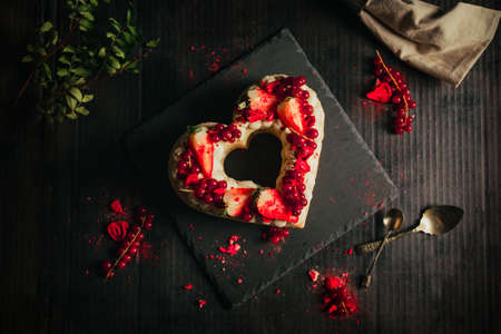 Confectionery concept - red and white cake in heart shape for St. Valentine's Day on black table (plate). Sweet and romantic present - Strawberry Cake on dark black background.の写真素材