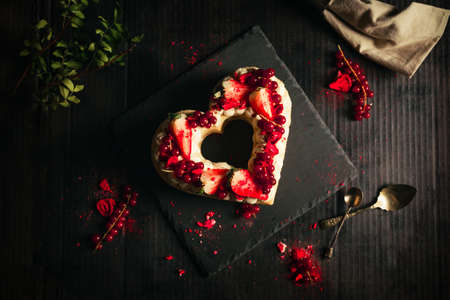 Confectionery concept - red and white cake in heart shape for St. Valentine's Day on black table (plate). Sweet and romantic present - Strawberry Cake on dark black background.の写真素材