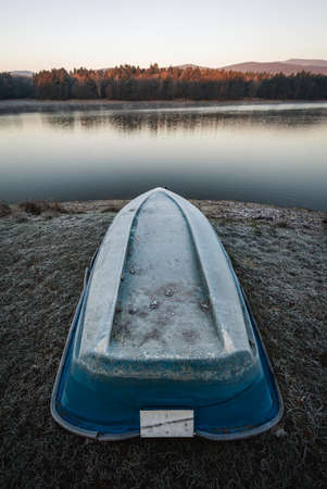 Mole (pier) with boat on the shore of cold lake on sunrise - autumn time.  Landscape scenery - forest and lake on morning sunrise with beautiful orange sunlight.の写真素材