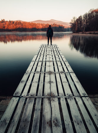 Man (tourist) standing on the frozen mole (pier) with water reflection in lake. Traveler with...