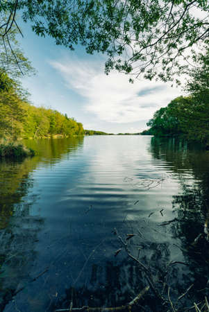 Vertical photo of Nemecky lake (pond) in Slovakia (Europe) with reflection in water and green beautiful forest. Reservoir with smooth waves in water surrounded by green trees.の写真素材
