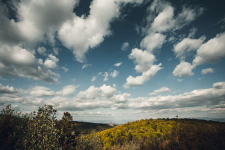 Dramatic and big white clouds on the crystal blue sky over the green hills in spring.  Perfect and moody spring landscape with green hills and forest on background. Natural light on dramatic sky.の写真素材