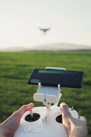 POV view - Man control the drone by remote control over the meadow on sunset. Man operating the drone and flying over the field with hill on background in springtime.の写真素材