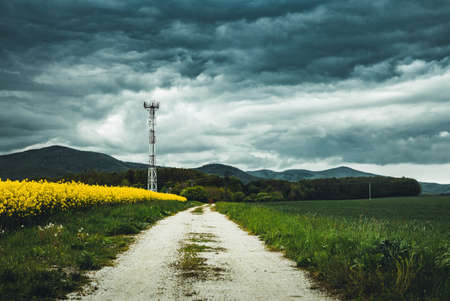 View of landscape and road before the storm with signal tower on the field with dark cloudy sky....