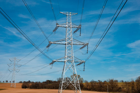 Electrical substation utility pole, state and high voltage power line silhouette with blue cloudy sky at sunset. View of  illuminated transmission tower on field in spring  with a lot of cables.の写真素材