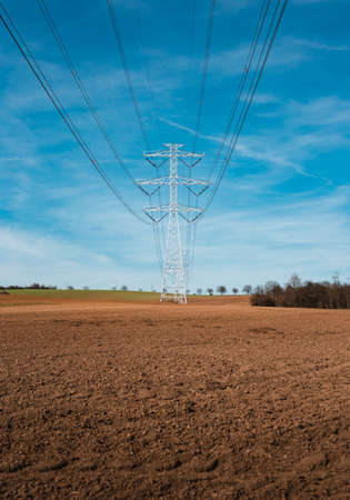 Electrical substation utility pole, state and high voltage power line silhouette with blue cloudy sky at sunset. View of  illuminated transmission tower on field in spring  with a lot of cables.の写真素材