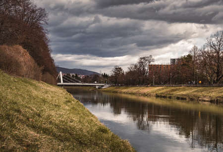 Image - City in Slovakia (Nitra) with Nitra river with bridge on background - stormy weather. Photo of park  in the middle of European city. Dark landscape photo in spring before a storm.の写真素材