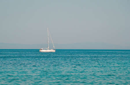 Yacht sailing on opened sea with hills on background. Sailing boat floating on sunnyday- Image. Sailing boat on sea with crystal blue water.  Beautiful scenic photo of boat on the sea.の写真素材