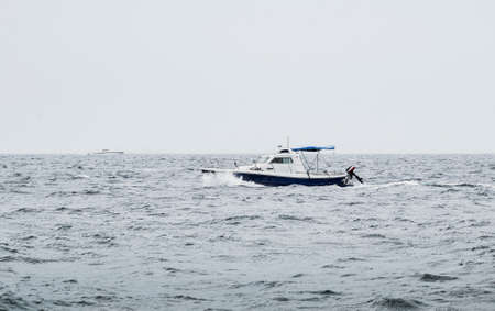 A motorboat floating on the heavy sea with waves in bad weather conditions with other luxury yacht on background.   Boat on the ocean (overcast day) after the storm - imageの写真素材