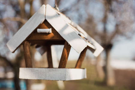 Wooden birdhouse hanging on the tree with a lot of other trees and blue sky on background. White Close up photo of nesting box in the garden (with bokeh effect)の写真素材