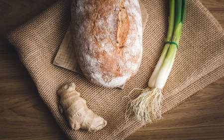 Illuminated handmade bread  on wooden table wwith jute decor.  Close up photo of Homemade bread with bunch onion and ginger (top view).の写真素材