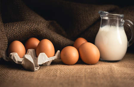 Photo of raw illuminated eggs  in kitchen with jute on dark background. Close-up photography of bio chicken eggs in egg box with milk in a ewer glass.の写真素材