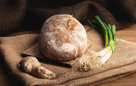 Illuminated handmade bread  on wooden table with jute decor.  Close up photo of Homemade bread with bunch onion and ginger.の写真素材
