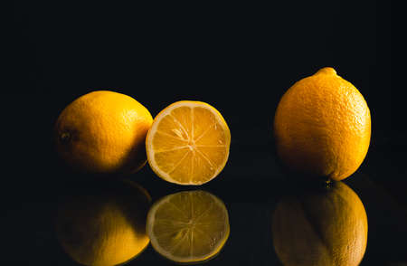 Photo of illuminated lemons with reflection on dark background. Three isolated yellow lemons on black background with mirroring effect.の写真素材