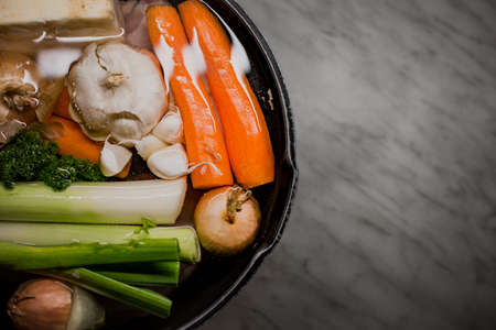 Clear Chicken broth with pieces of  vegetables in a metal pot before cooking with crystal water.  Chicken Soap with a lot of vegetables in preparation process  in a saucepan with free and empty place for textの写真素材