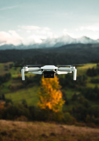 Close up photo of small white drone flying in the air with beautiful scenic view of the green meadows and snowy mountains on background. Vertical detailed photo of drone (uav) in colorful scenery.の写真素材