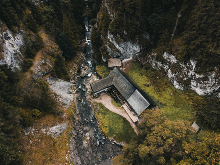 Photo of a beautiful wooden cabin with river in the forest from above - Mlyny Oblazy (Slovakia) - taken by drone. Old wooden mill with rocks on background in autumn time. - aerial photography.の写真素材