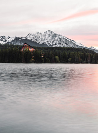 Vertical photo of beautiful lake in autumn scenery with amazing snowy mountains on background. Strbske pleso in High Tatras in fall with water reflection at sunrise.の写真素材