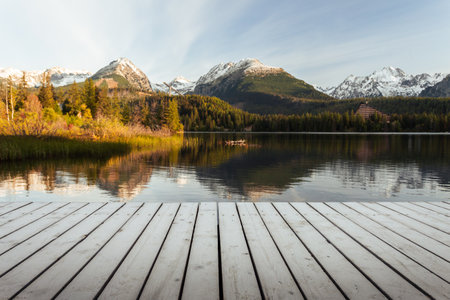 Mole (pier) on the lake in autumn scenery with beautiful and snowy mountains on background. Strbske pleso in High Tatras in fall with wooden mole and water reflection of landscape at sunrise.の写真素材