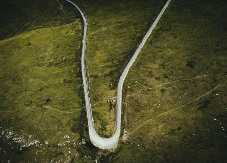 Aerial photo of mountain curved roadunder the mountain peak in  Europe. Alpine road - beautiful scenic landscape with green meadows and rocks from above. Dark and moody photo of a way in mountains.の写真素材
