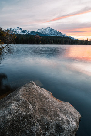 Vertical photo of beautiful lake in autumn scenery with amazing snowy mountains on background. Strbske pleso in High Tatras in fall with water reflection at sunrise.の写真素材