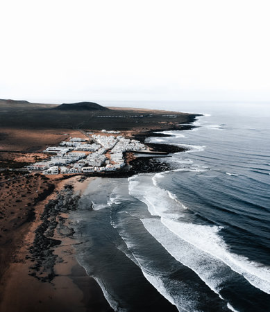 Aerial photo of Caleta de Famara in Canary Islands - Lanzarote. Moody and dark style of wide photo from above with strong waves in blue ocean and white clear sky. Cliffs and rocks with ocean by drone.の写真素材