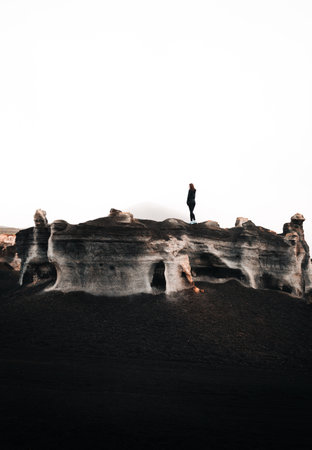 Minimalistic vertical photo of woman tourist standing on the top of rock in desert. Stratified rocks (teseguite - Lanzarote) with traveler on top in dramatic and moody atmosphere.の写真素材