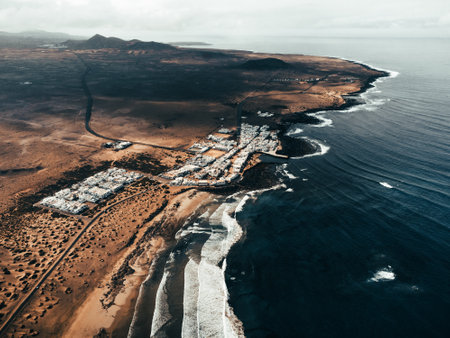 Aerial photo of sunset on Caleta de Famara in Canary Islands - Lanzarote:  wide photo from above with strong waves in blue ocean and white clear sky. Cliffs and rocks with ocean by drone.の写真素材