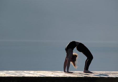 Girl practicing her yoga on a pier by a lakeの写真素材