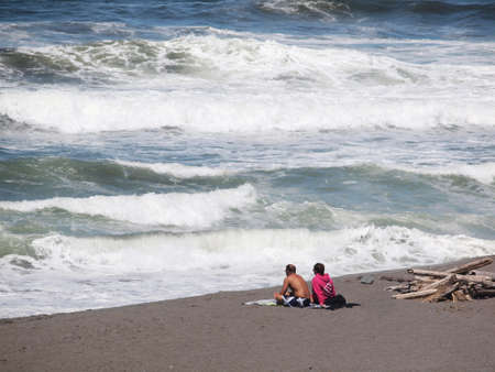 Couple sat on an Oregan beach in Windy weather watching the waves and enjoying the viewのeditorial素材