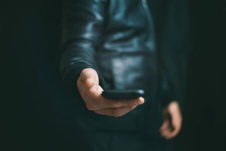 Young Male Hand holding Black Smartphone. Soft Focus. Dark room. New Technologies, Trends among young people, Hacking, Internet Security Concept. Modern Technology: Advantages and Disadvantagesの写真素材