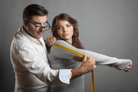 The young tailor takes measures of a young woman with measuring tape and he shows itの写真素材